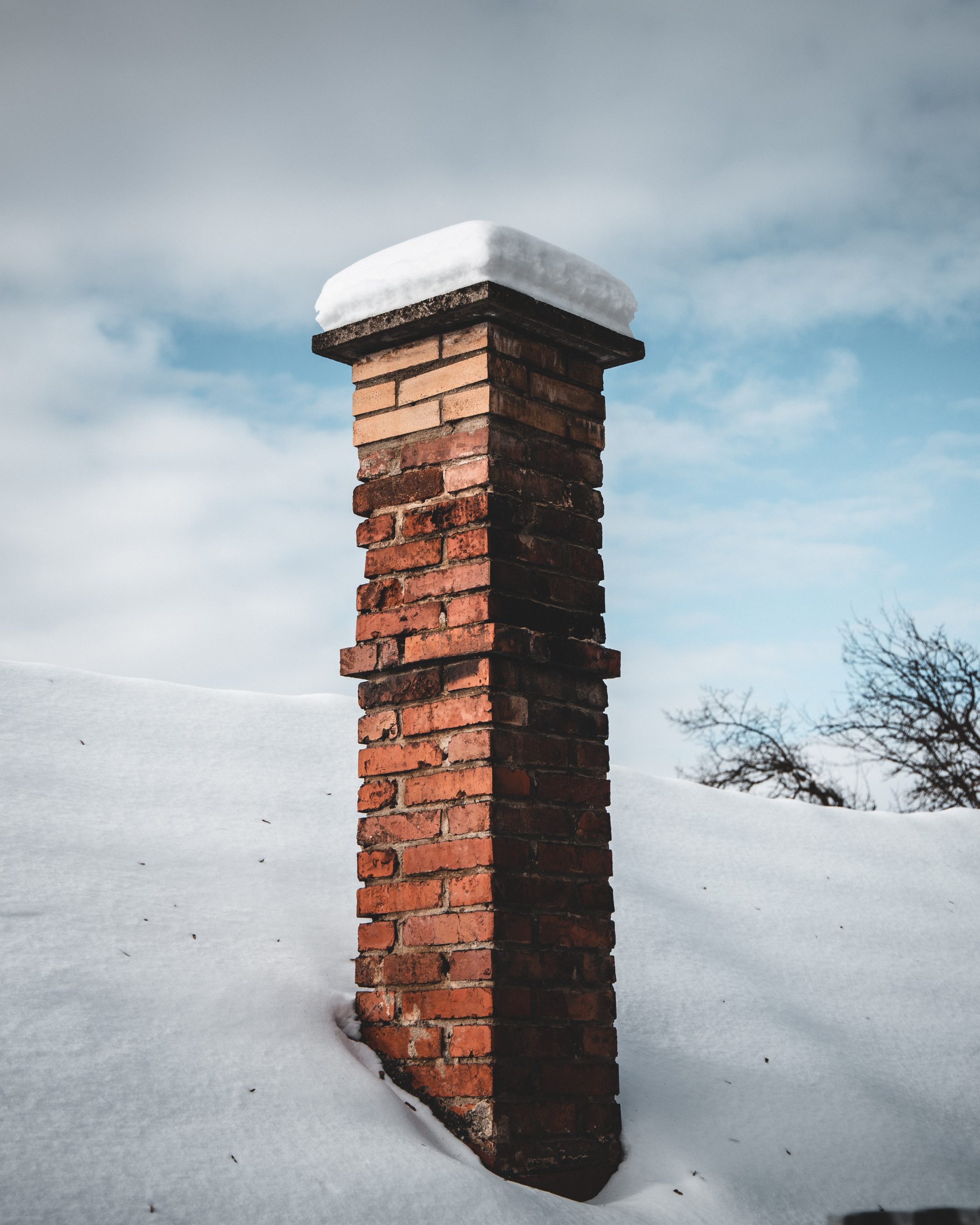 Vertical shot of snowy roof with a chimney under the cloudy sky